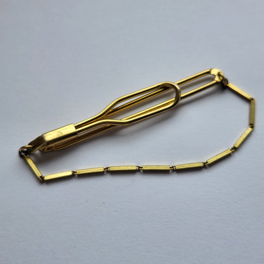 Detailed view of a gold-tone tie clip, marked TEKA.